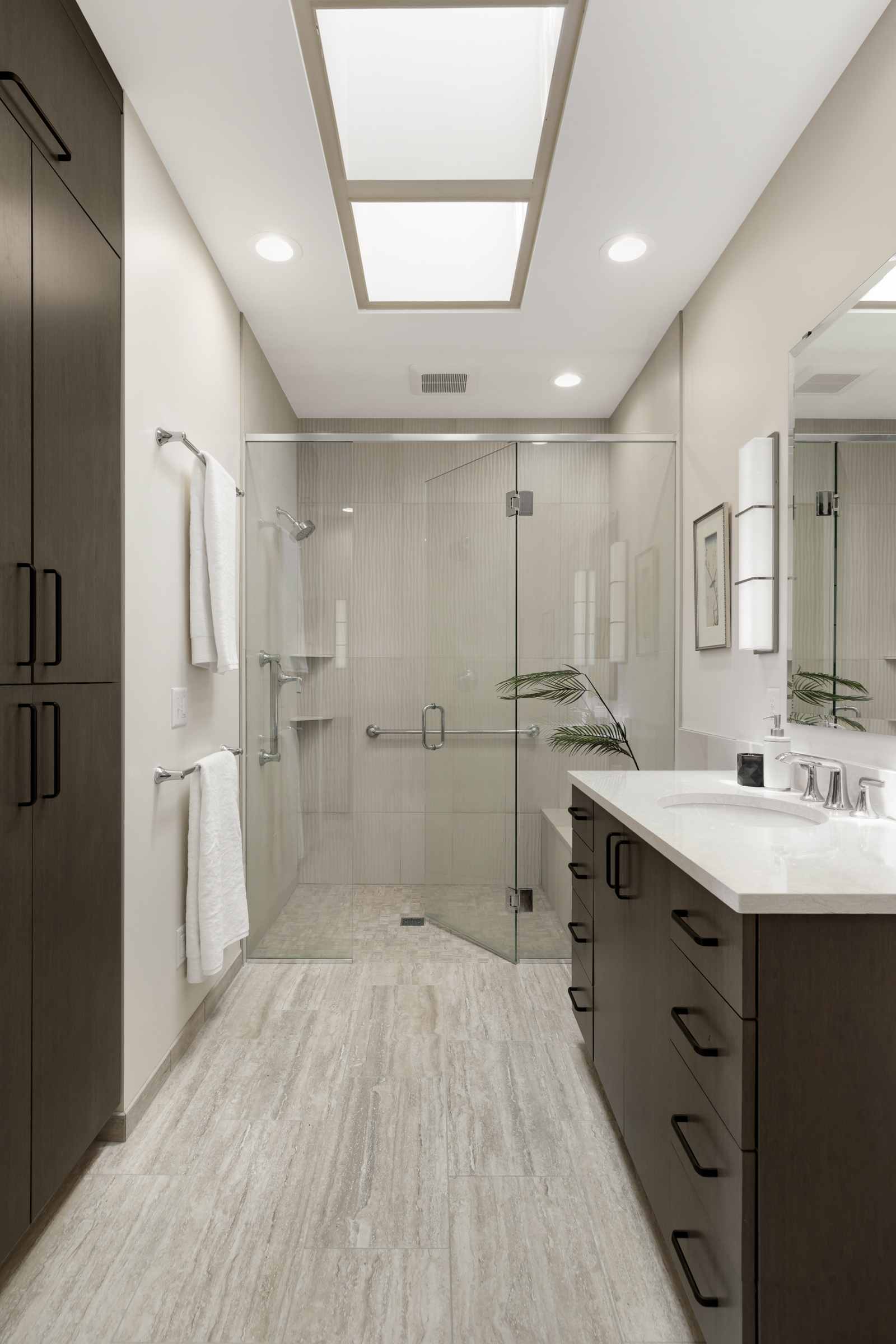 Bathroom remodel with skylights, walk in glass shower, and dark wood cabintry
