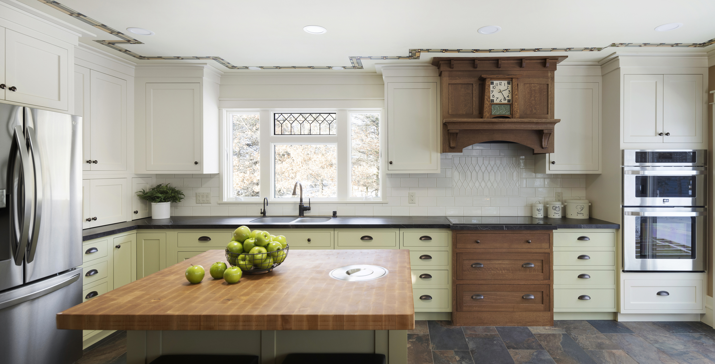 Kitchen with natural wood stove hood, light green base cabinets, and white upper cabinets