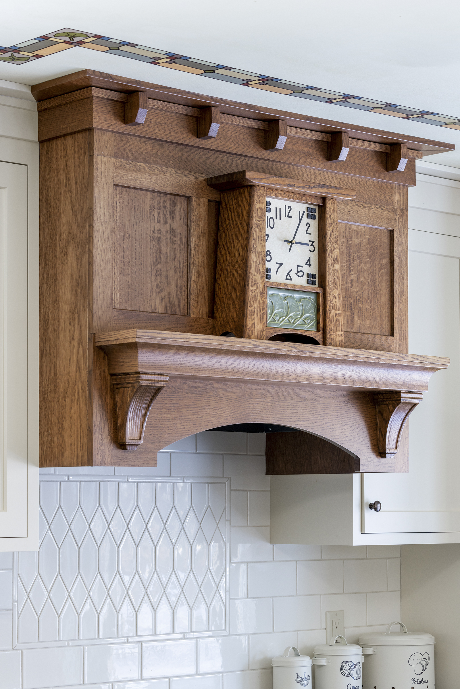 Kitchen remodel with white tile backsplash above stove top with custom wooden hood vent