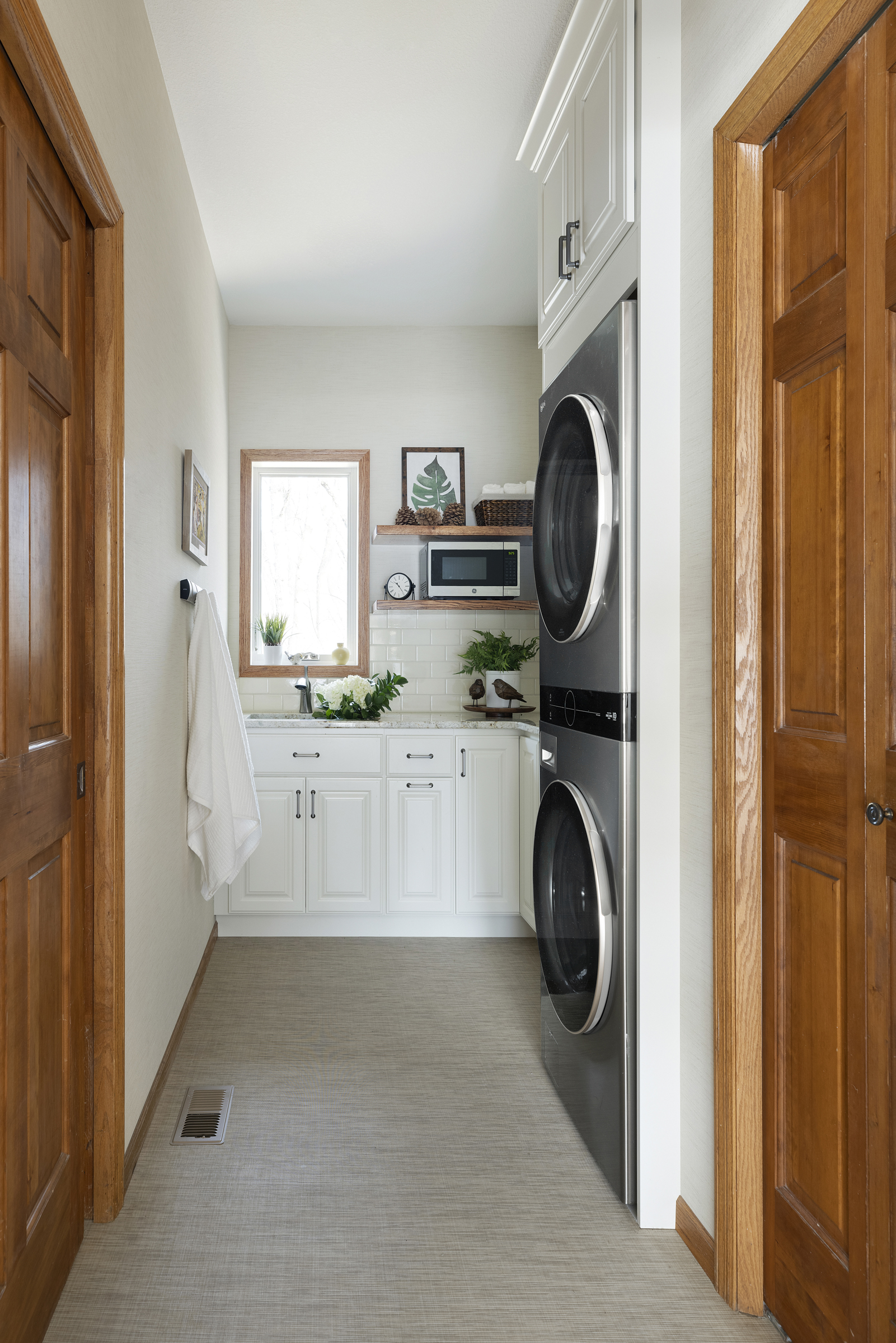Remodeled laundry room with wooden doors, white cabinets, and stacked washer/dryer