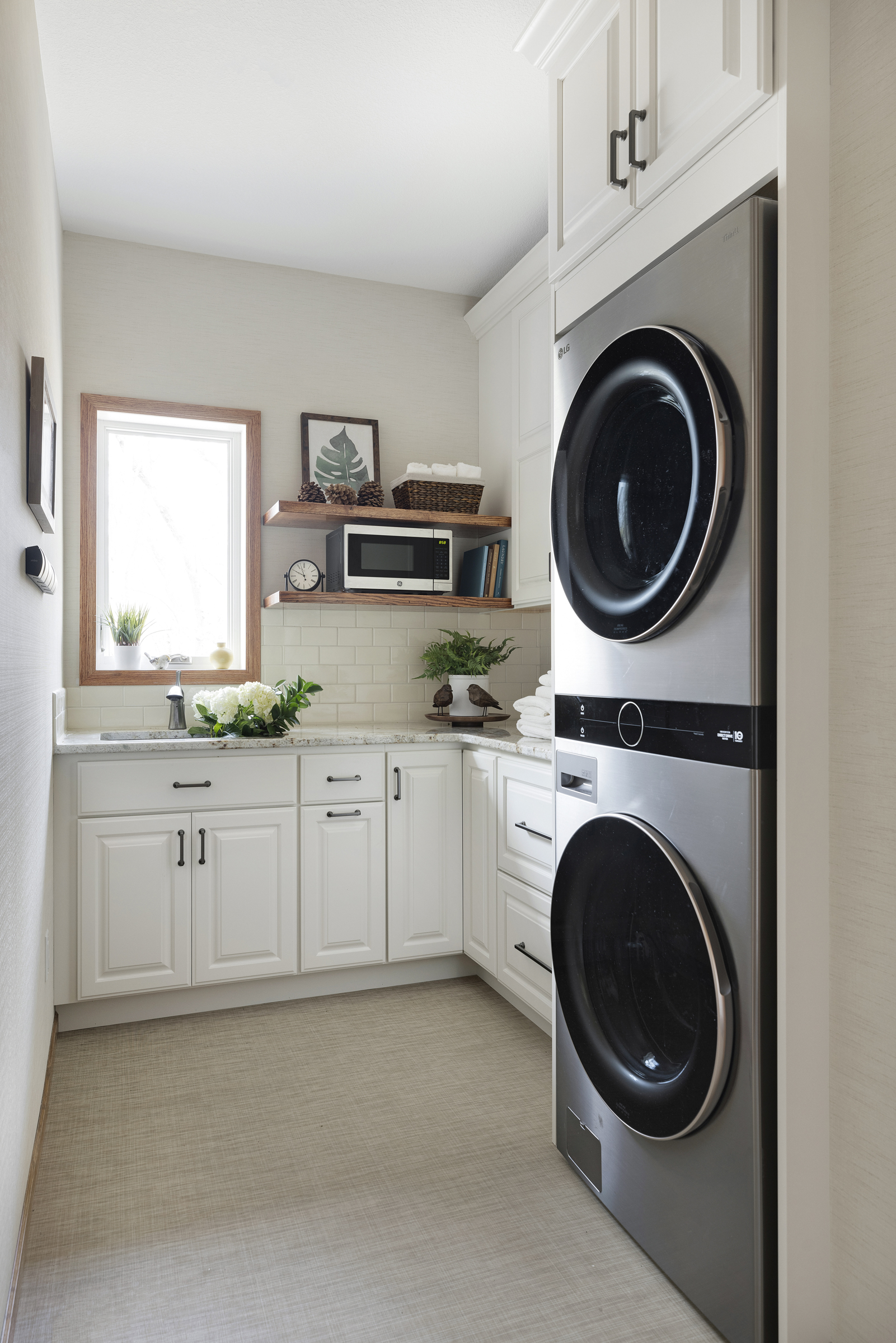 Laundry room after remodel with stacked washer and dryer, white cabinets, and subway tiles