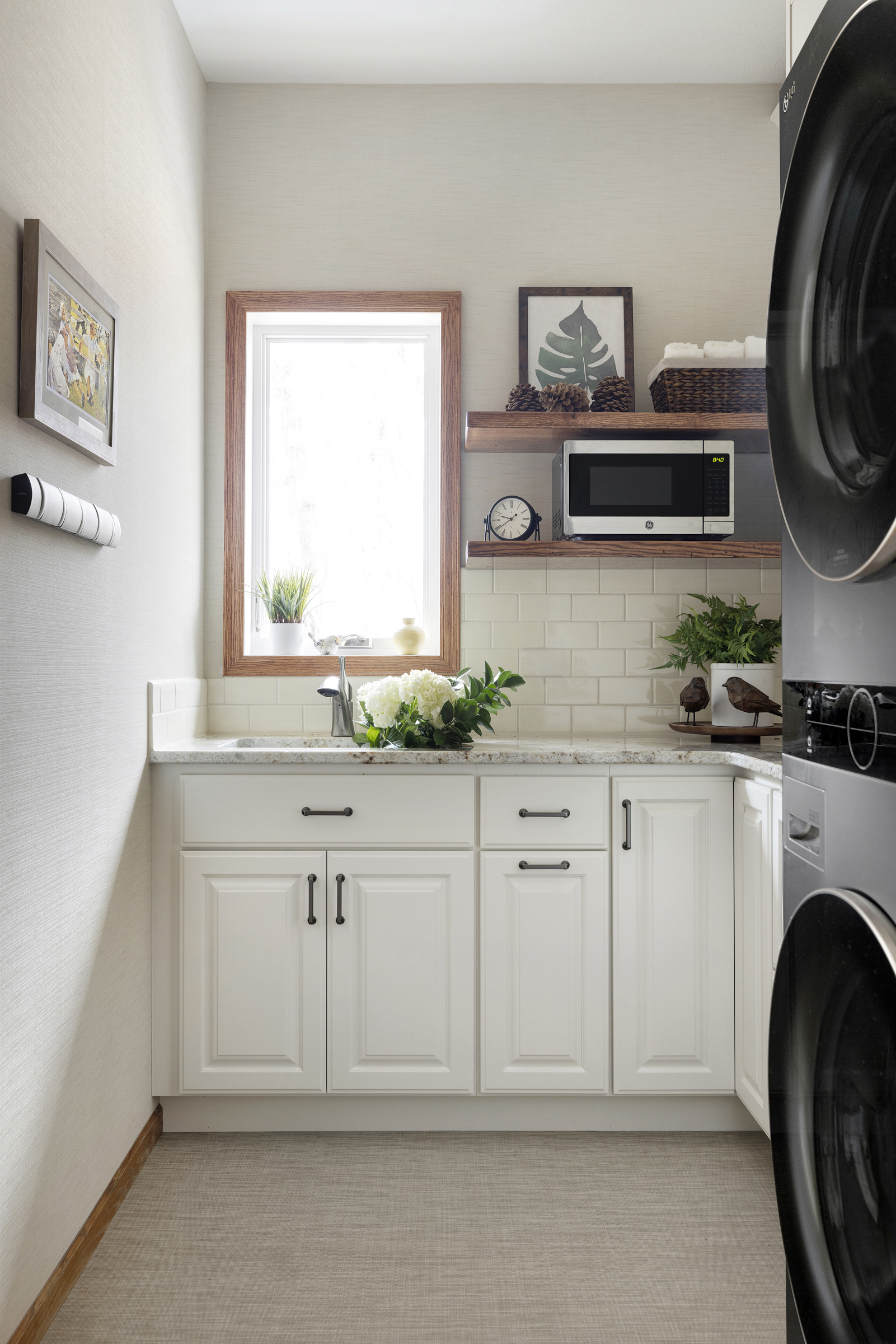 Remodeled laundry room with white cabinets, white subway tile, and window over sink