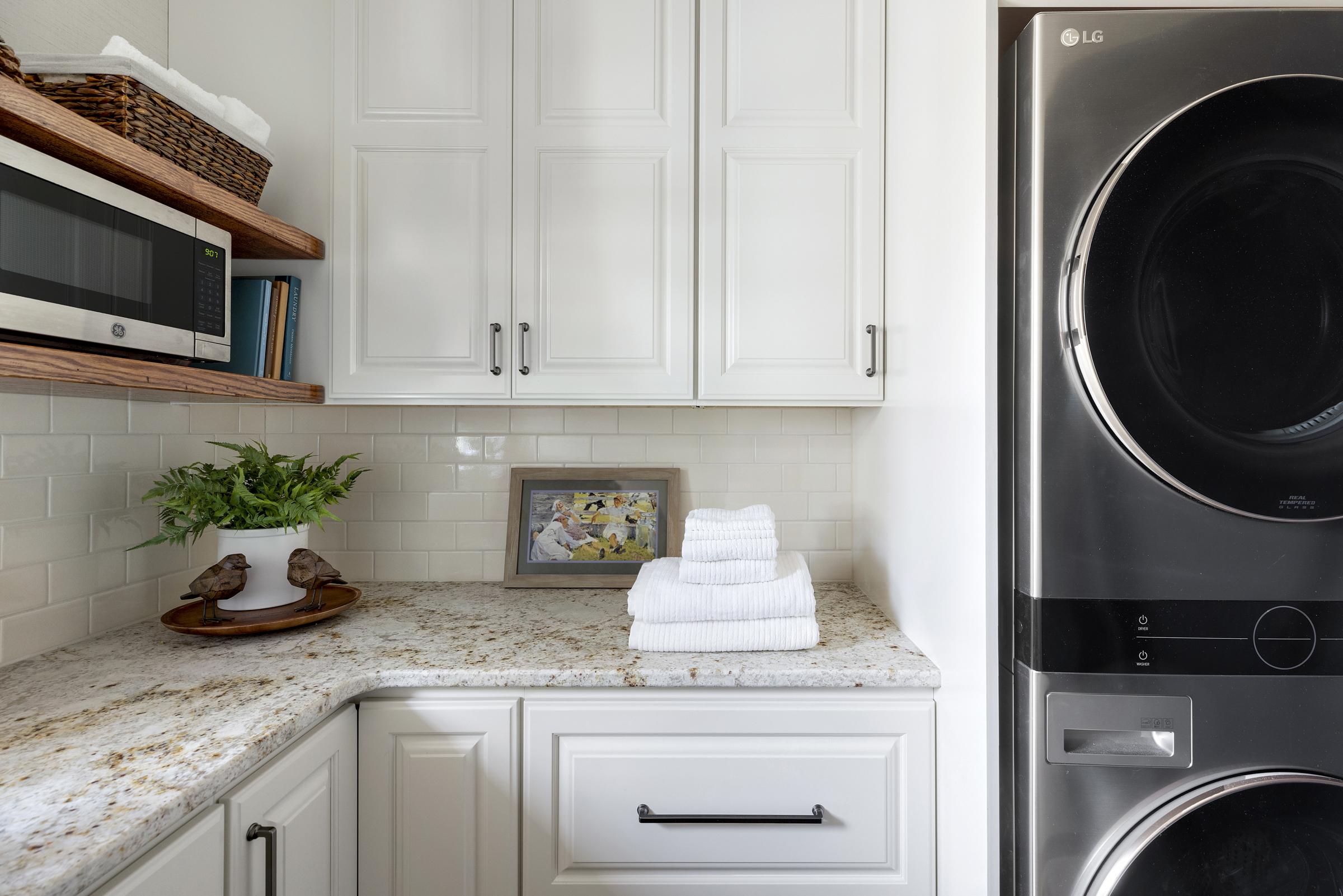 Laundry room model with stacked washer and dryer, white subway tile, and wooden floating shelves