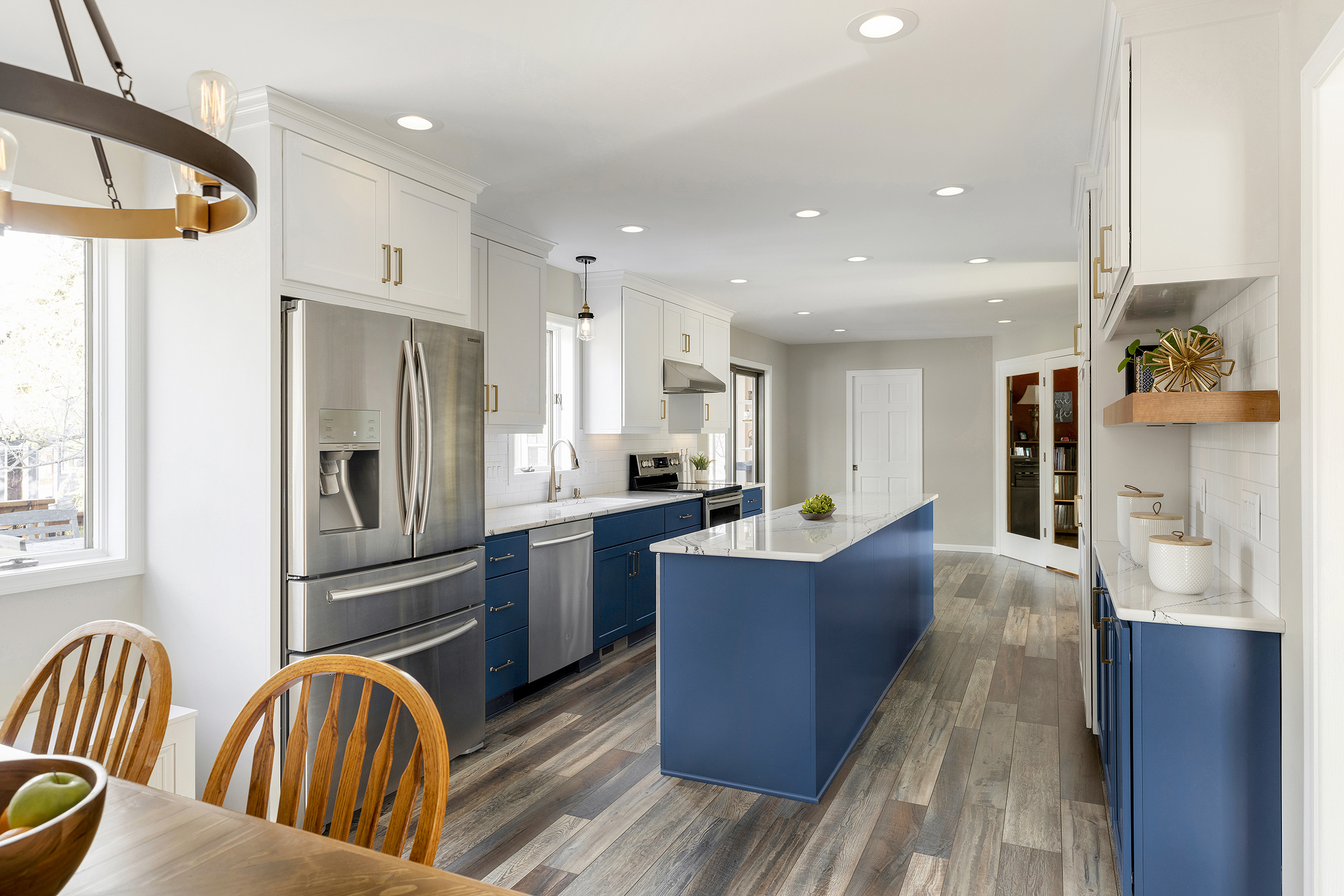 Remodeled kitchen with blue base cabinets, large island, brick wall, and gold fixtures