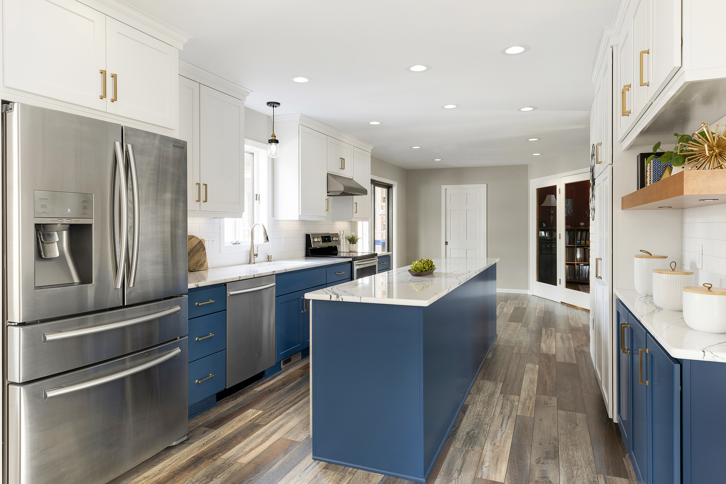 Kitchen remodel with large blue island, white marble counters, wooden floating shelf, and gold handles