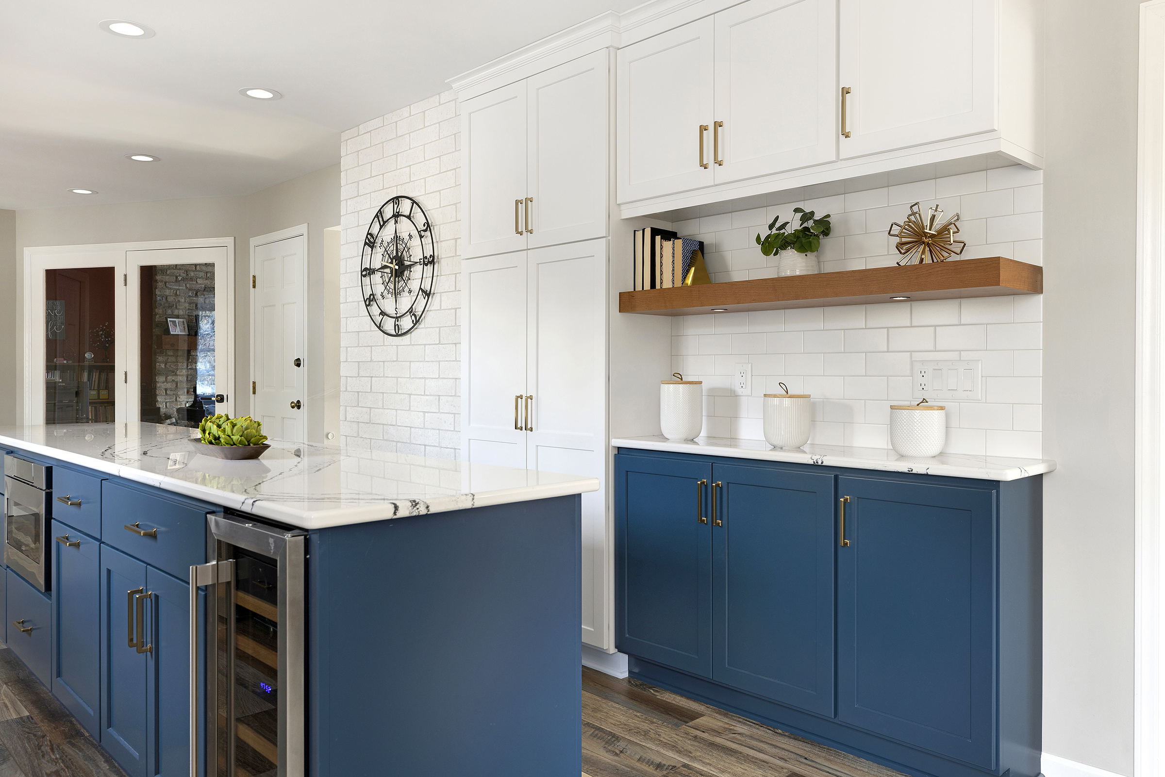 Kitchen remodel with blue base cabinets, white tall cabinets, floating wood shelf, and white subway tiles