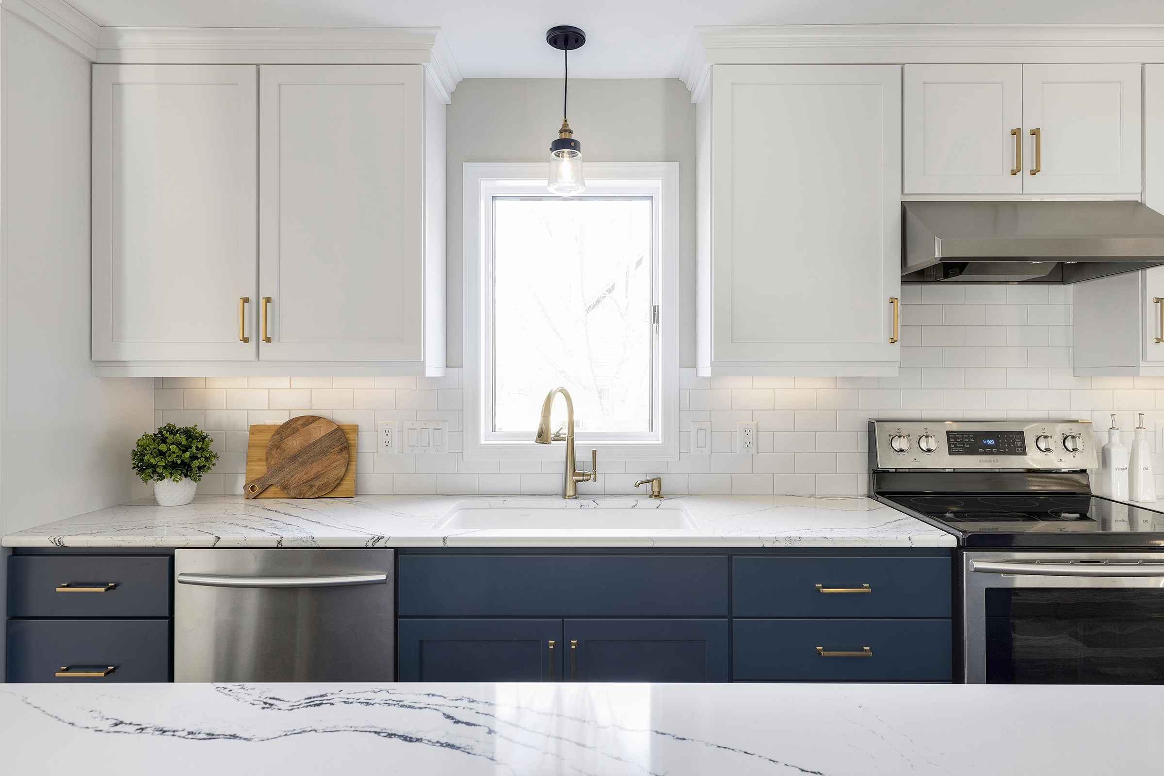 Renovated kitchen with white upper cabinets, blue lower cabinets, and window over sink with light