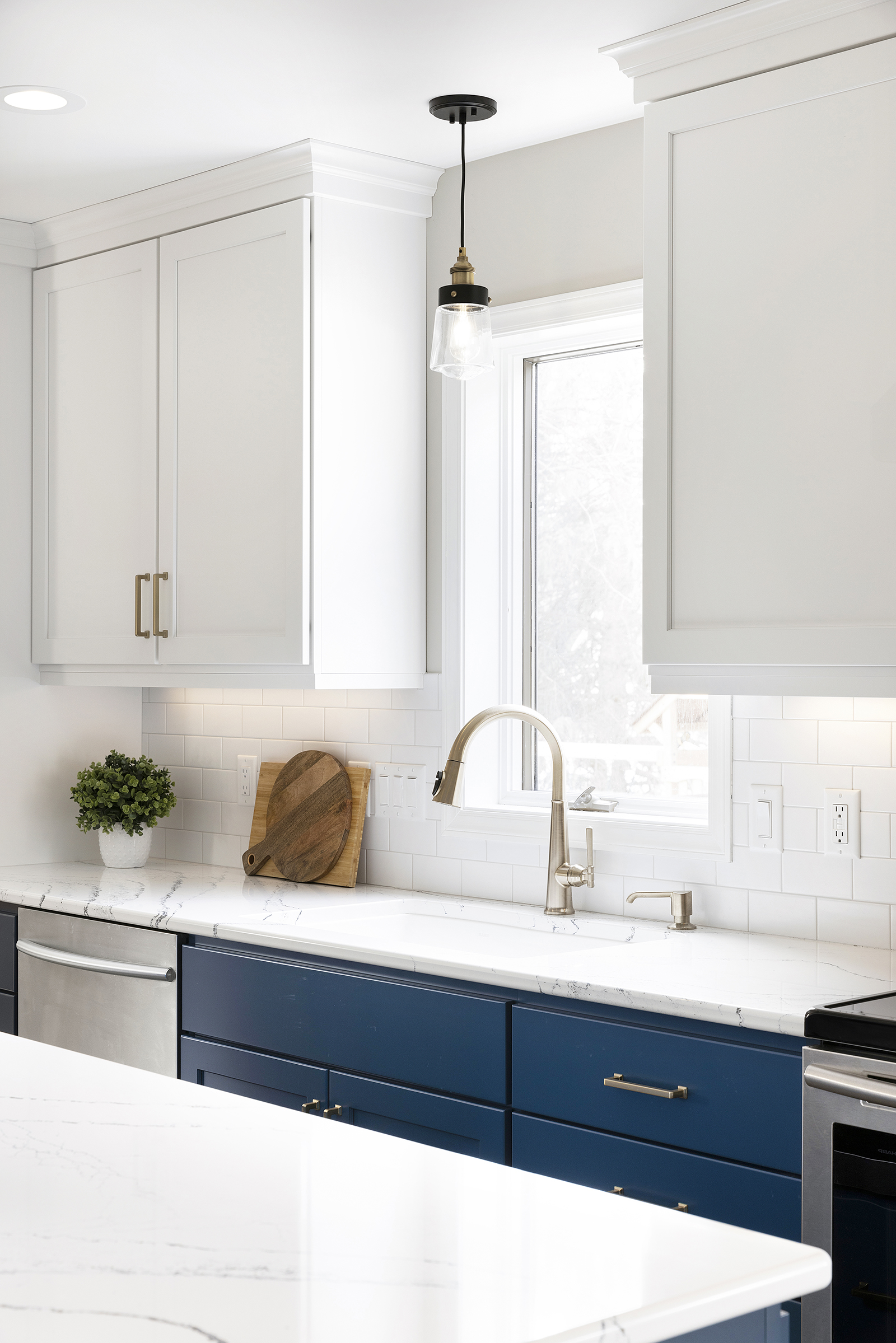 Renovated kitchen with blue base cabinets, white upper cabinets, and sink with window and light