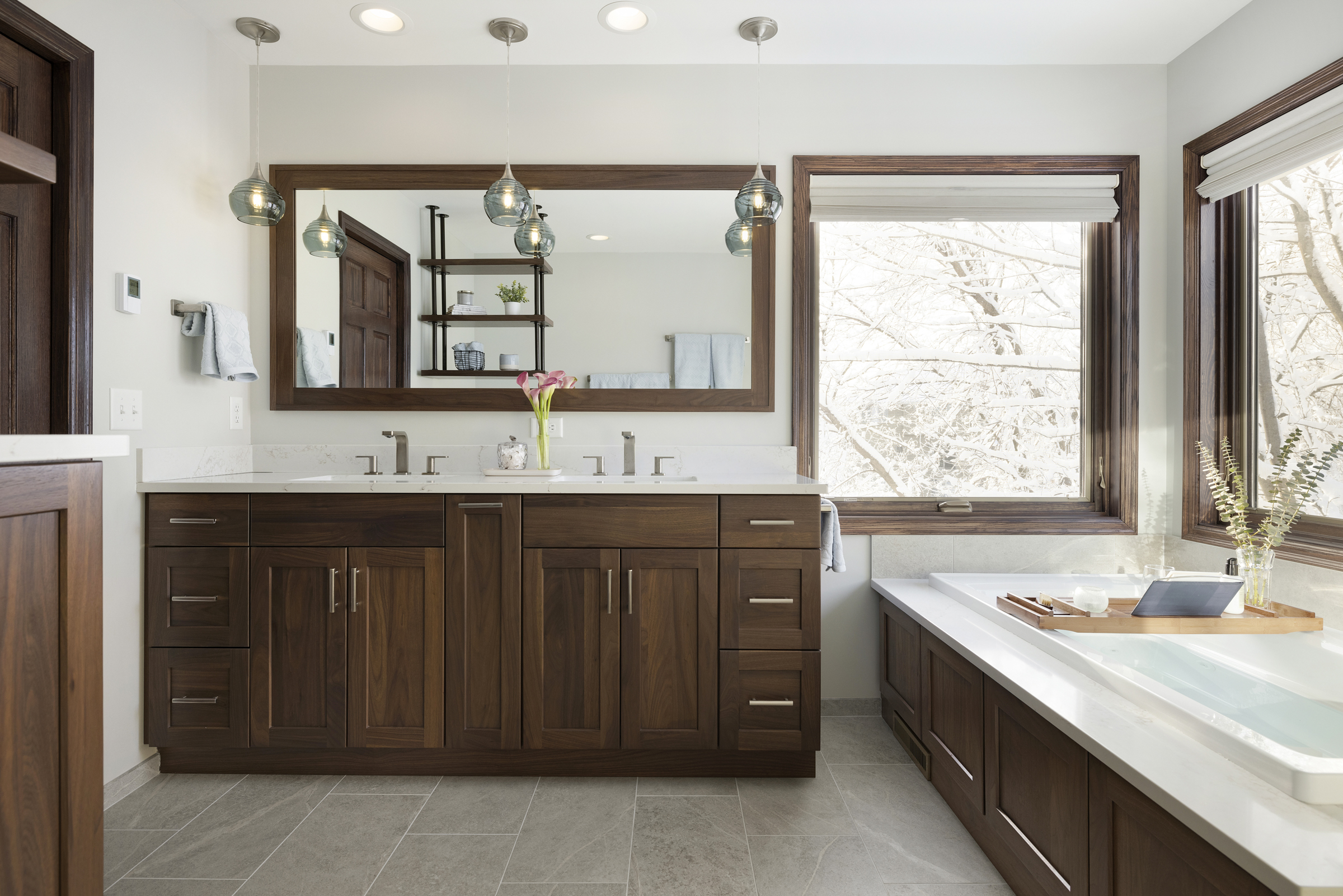 Primary bathroom remodel with dark wood cabinet and trim and large bathtub under windows