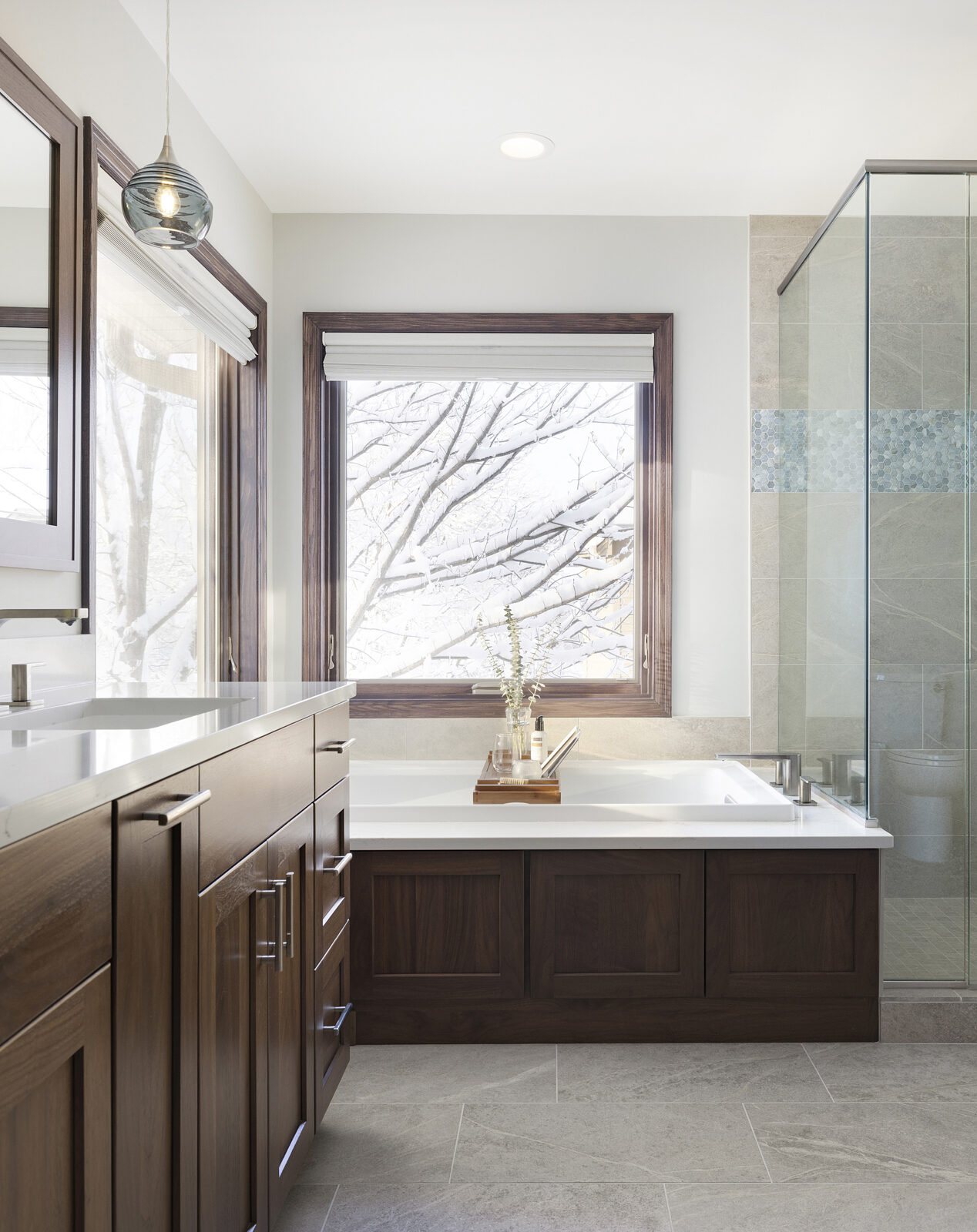 Primary bathroom remodel with dark wood cabinet and trim and large bathtub under windows and glass-enclosed shower