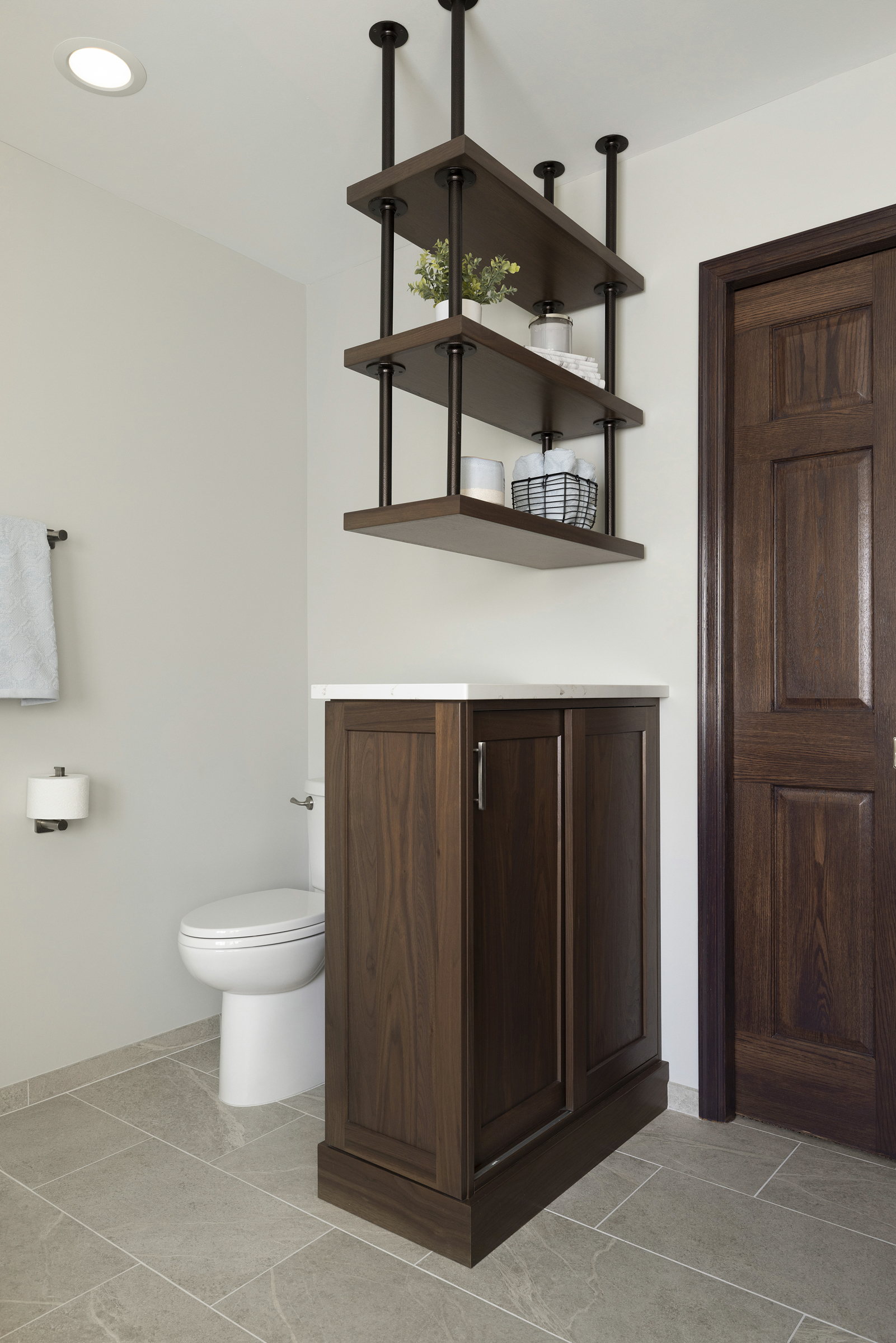 Primary bathroom renovation with dark wood cabinet and trim with shelves handing by metal bars from ceiling separating toilet area