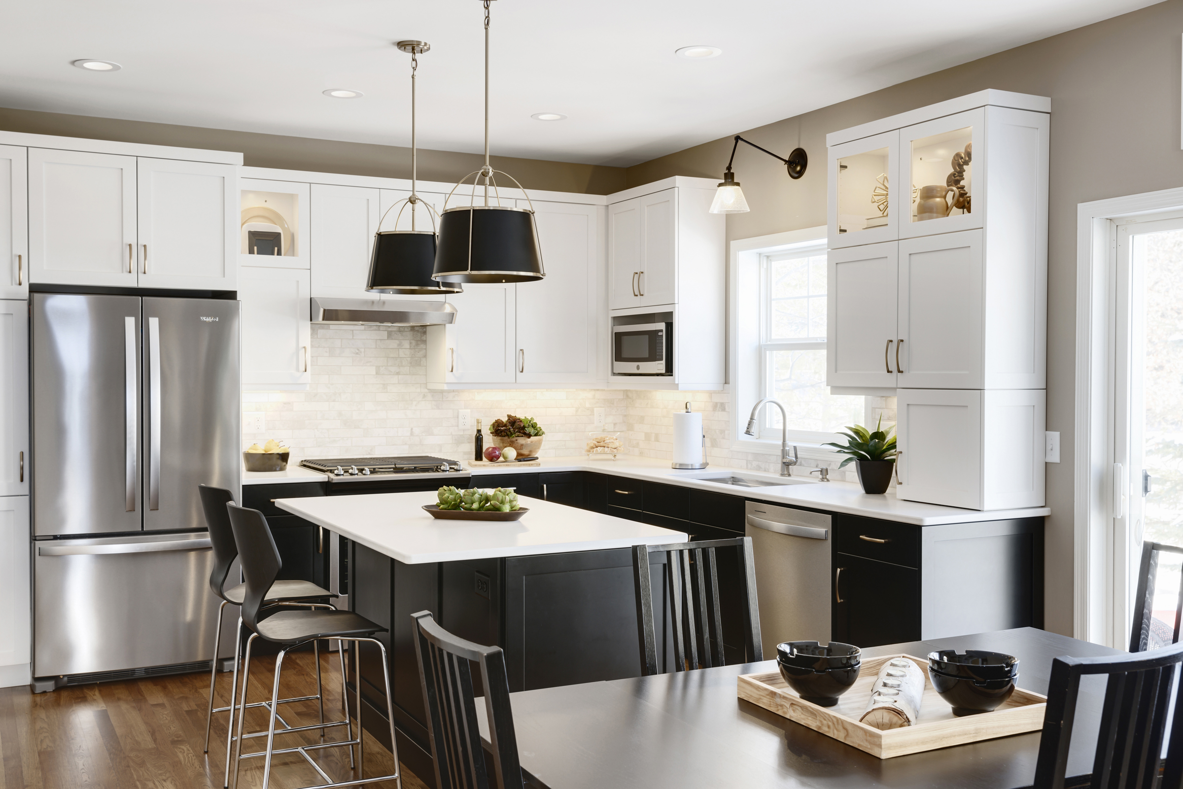 Bold kitchen renovation with black base cabinets, white upper cabinets, wood floor, and large island