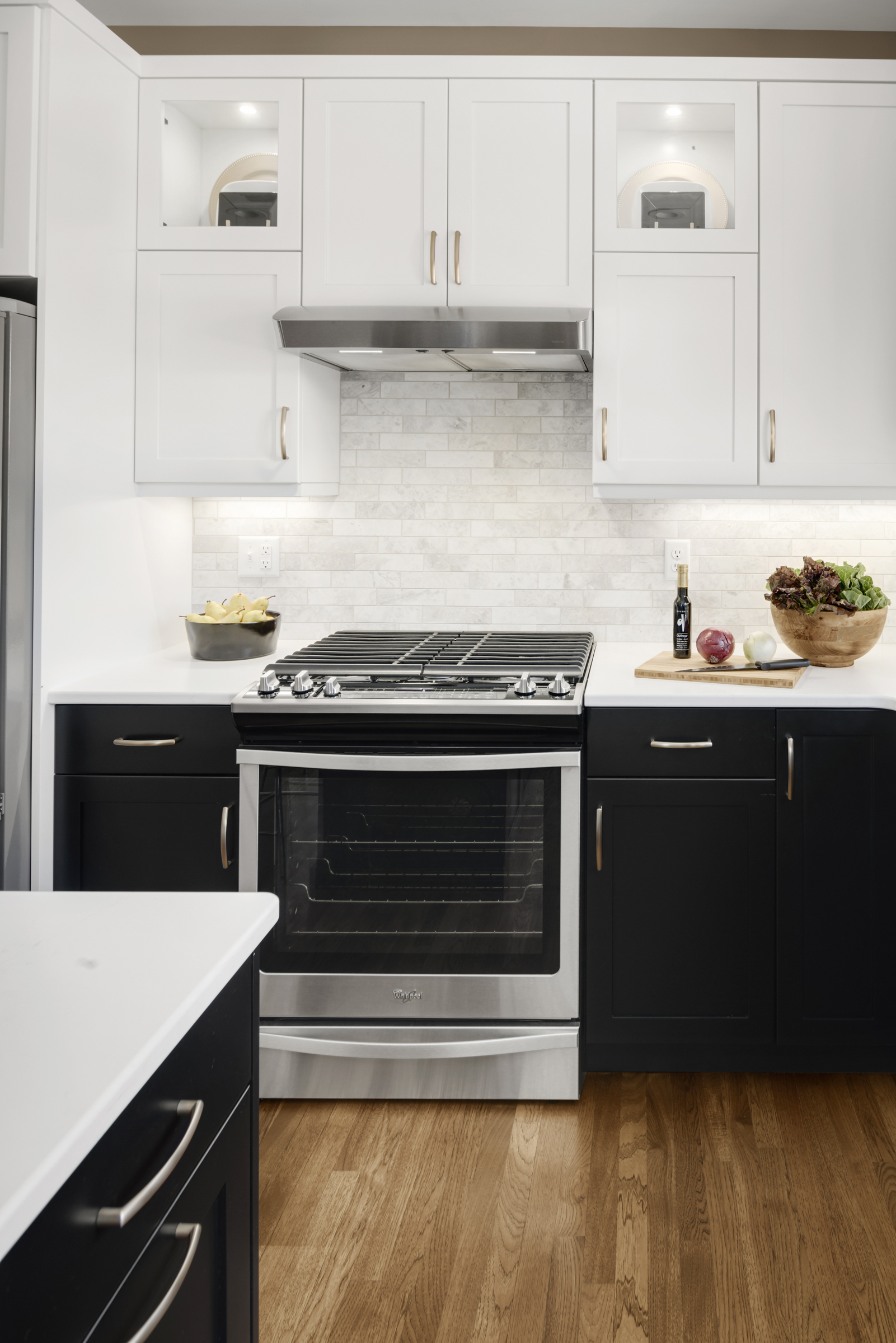 Bold kitchen renovation with black base cabinets, white upper cabinets, wood floor, and large island