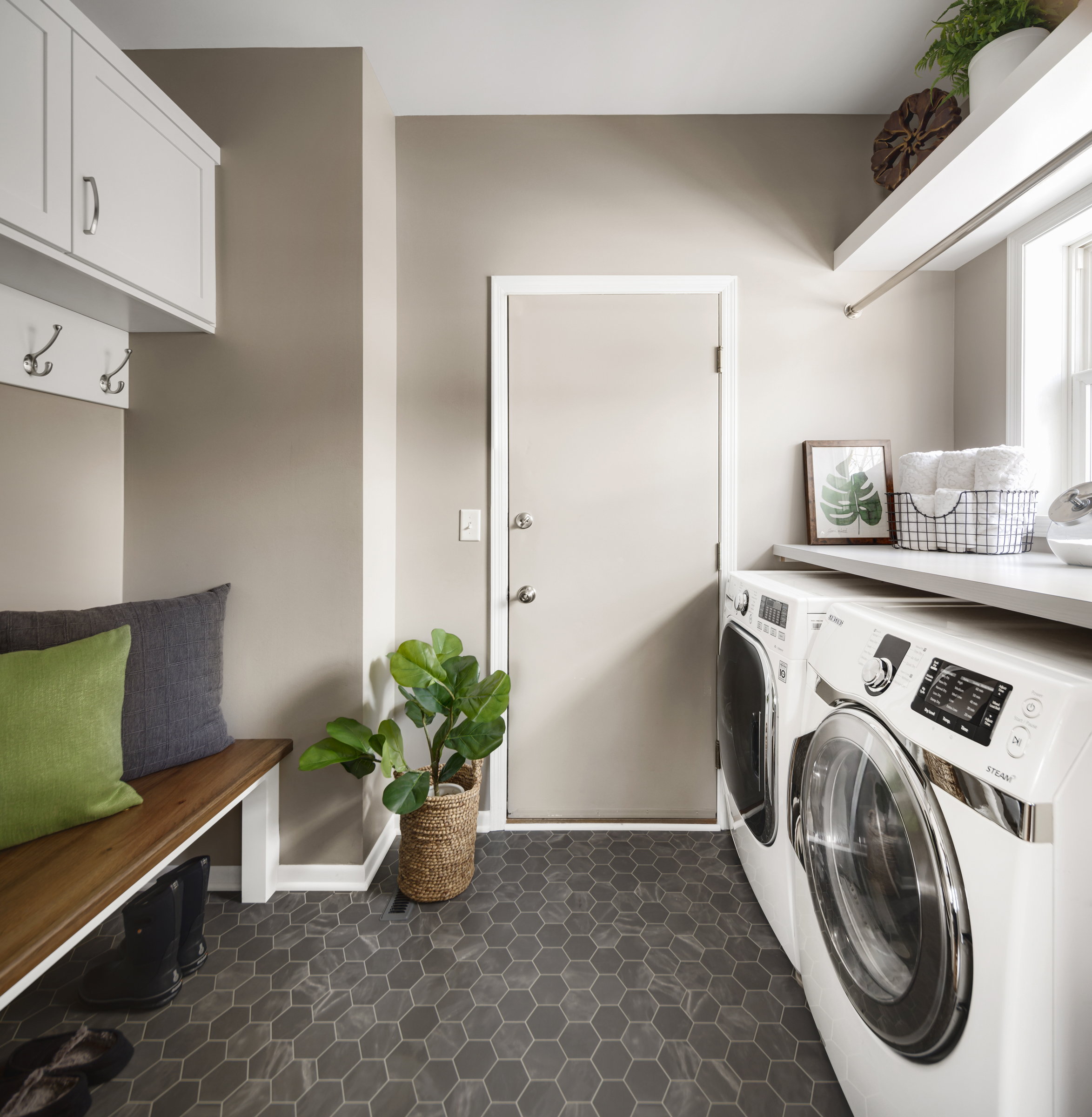 Bold laundry room renovation with dark tile floors, tan walls, and white cabinets