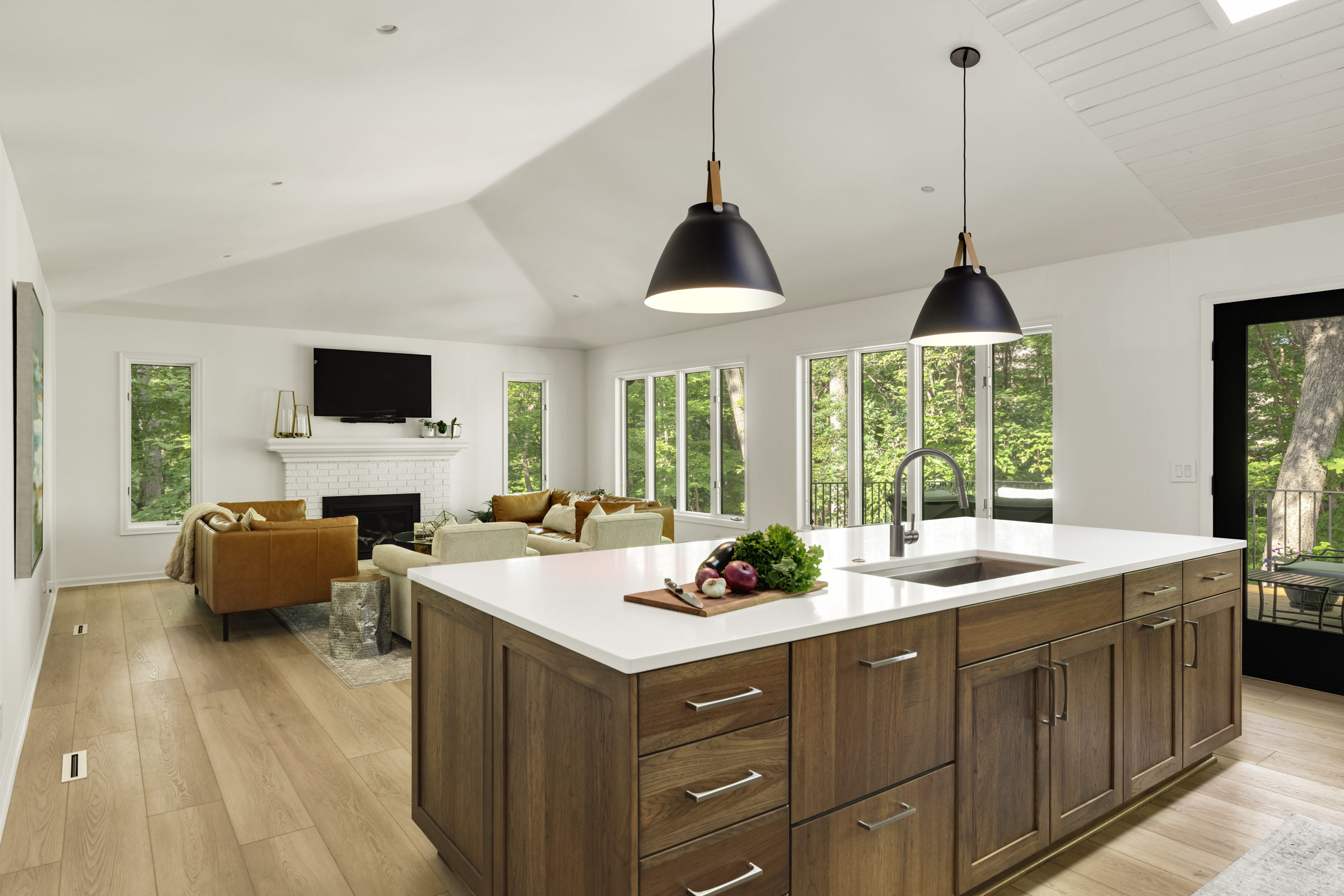 Kitchen remodel opened up to living room, with light wood floor, darker wood cabinets, and pendant lights