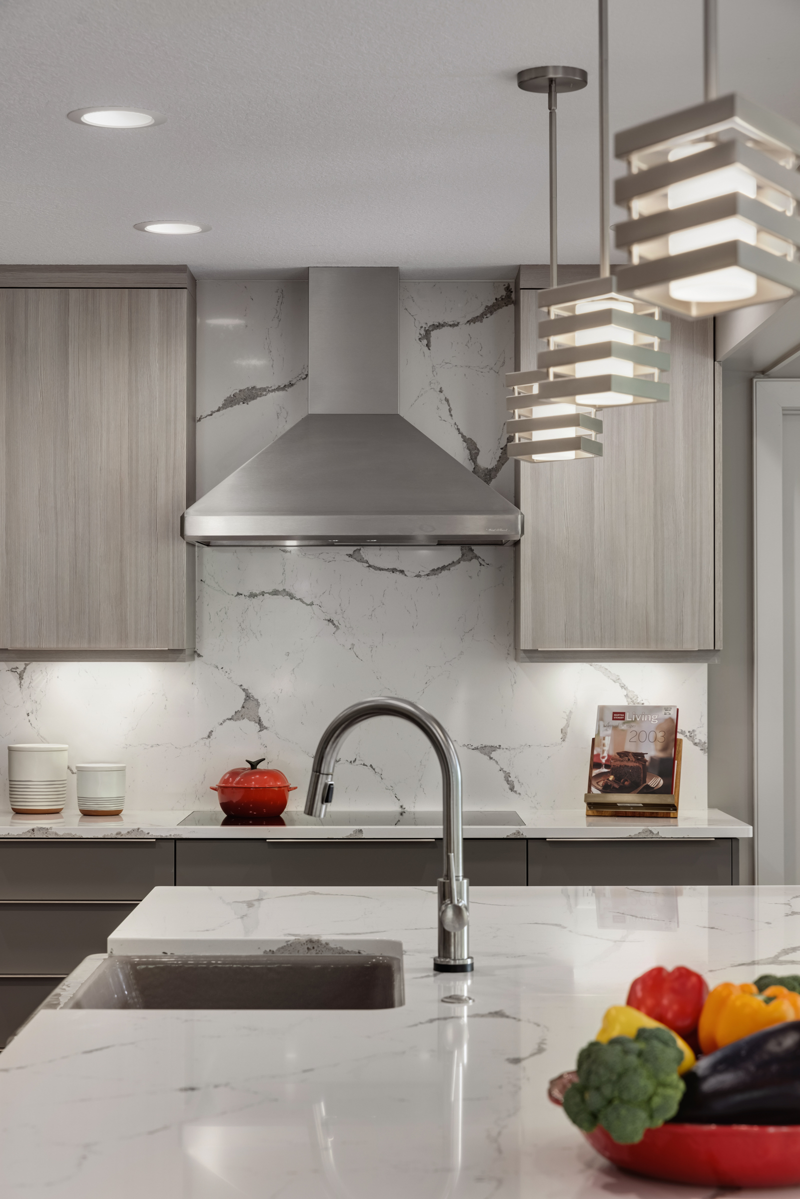 Contemporary kitchen remodel with stainless hood, light wood cabinets, and full height marble backsplash