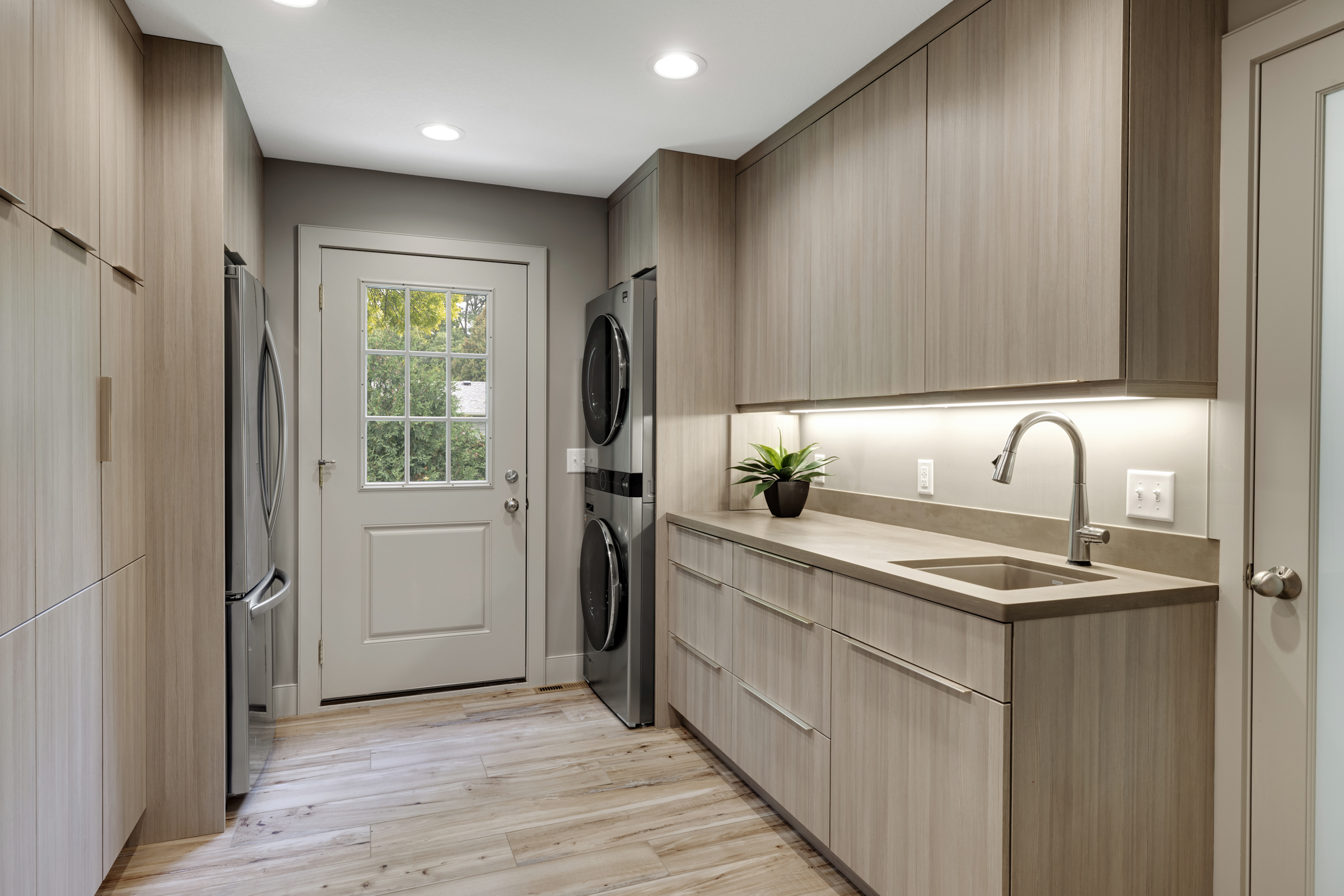 Contemporary laundry room with light wood floor, light wood cabinets, and plenty of storage
